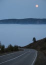 The road goes down into the clouds and fog in the mountains and the orange moon in the sky Royalty Free Stock Photo