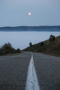 The road goes down into the clouds and fog in the mountains and the orange moon in the sky Royalty Free Stock Photo