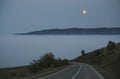 The road goes down into the clouds and fog in the mountains and the orange moon in the sky Royalty Free Stock Photo