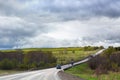 Road goes far away into the distance, horizon, few cars, green field and forest, cloudy blue sky background Royalty Free Stock Photo