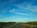 A road or highway leading to the horizon. View from the car window. Northern dim summer, blue sky with white clouds Royalty Free Stock Photo
