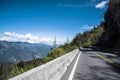 Road on the hill side running through forest with mountains, blue sky, and clouds. Royalty Free Stock Photo