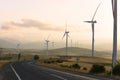 Road among hilly terrain with wind turbines and mountains Royalty Free Stock Photo