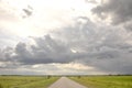 Road in Holland countryside, perspective, under heavy dark threatening cloudy skies and between meadows and a faraway straight