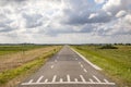 Road in Holland with white cycle path lines on both sides, perspective, under heavy threatening cloudy skies and between meadows