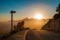 Road with an index post down into the valley against the background of the mountains range  on the horizon with the sunrising.. Royalty Free Stock Photo