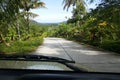 Road through jungle, view behind windshield of car. Palm trees and sea in background Royalty Free Stock Photo