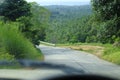 Road through jungle, view behind windshield of car. Palm trees and sea in background Royalty Free Stock Photo