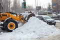 Road machinery clears snow piles from city streets on a winter day