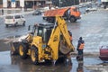 Road maintenance workers in orange vests stand near a tractor that cleans snow.