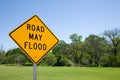 Road May Flood Sign Against A Blue Sky, Green Trees and Grass