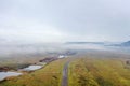 Road in the middle of a green field under a foggy and cloudy sky