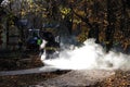 road mini building roller is working on the repair site of the bike path next to the sidewalk. white vapor glows in the sun.