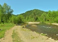 The road running along the edge of the forest along the bank of a small mountain river on a clear sunny day