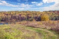 A road in the rural field leading to the lake among lush vegetation. Surroundings colored autumn yellow, red, golden and orange Royalty Free Stock Photo