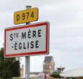 road sign with name of place and the church with bell tower which became symbol of the Normandy landings in France Royalty Free Stock Photo