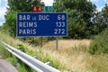 A road sign to the towns of Bar le Duc, Reims and Paris, 272 km away, on an abandoned highway among green trees and grass on the w