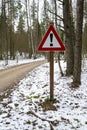 Road sign triangular shape with exclamation mark. Winter road in forest