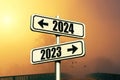 Road signs indicate the path to the new year 2024 and the old year 2023 on a blue sky with fog and sunset, creative idea. Choose a Royalty Free Stock Photo