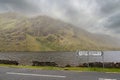 Road signs Leenaun and Louisburgh by a road. Beautiful scenery in the background. Mountains and low clouds and a lake. Connemara,