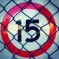 15 Road speed sign with red circle and chain link fence