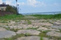 Road of stones overgrown with grass from the bottom angle against the river and blue sky Royalty Free Stock Photo