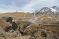 A road and tiny houses against the backdrop of yellow grass, snow-capped mountain peaks and rocky cliffs Royalty Free Stock Photo