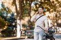 Road to work on eco transport. Guy walks with phone in park with bike