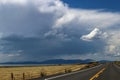 Road trip - Black top two lane highway stretches over the horizon past a barn and hay field by a lake towards the distant mountain Royalty Free Stock Photo