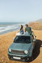 Road trip concept. Happy hippie couple on roof car and enjoying ocean view Royalty Free Stock Photo