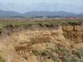 Sand Colored Jagged Cliffs Along the Californa Pacific Coast with Mountains in the Background