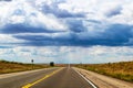 Road trip -Two lane highway on the plains stretches straight over horizonunder dramatic sky with strange light