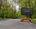 Road warning information sign on a trailer with LED face on suburban neighborhood street lined with trees that says MeToo
