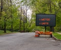 Road warning information sign on trailer with LED face on suburban neighborhood street lined with trees that says MeToo and Unit