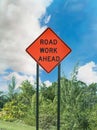 Road work ahead sign on the edge of the road under clouds