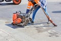 A road worker uses a petrol vibratory compactor, a vibratory roller, and an old broom to compact the asphalt on a stretch of road