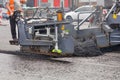 A road worker at the control panel of a tracked paver paver paving asphalt on a fenced road on a summer day