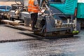 A road worker at the control panel of a tracked paver paver paving fresh asphalt on a fenced road on a summer day