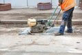 A road worker is patching up a pothole in an old road using an old petrol plate compactor