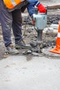 A worker using an electric jackhammer destroys the old asphalt near the sewer manhole