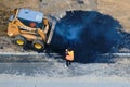 A road worker, a small bulldozer case and a large pile of hot asphalt, top view - Moscow, Russia, may 21, 2020