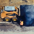 A road worker, a small bulldozer and a large pile of hot asphalt