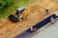 Road worker using a small bulldozer and workers with shovels