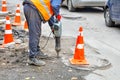 A road worker works with an electric jackhammer on a road section fenced with traffic cones