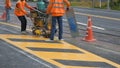 Road workers with thermoplastic spray road marking machine are working to paint traffic yellow lines Royalty Free Stock Photo