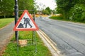 A roadwork sign against the backdrop of a broken road. Repair work of the road is underway.