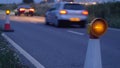 Roadworks cone flashing on UK motorway at night with traffic passing