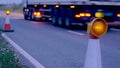 Roadworks cone flashing on UK motorway at night with traffic passing