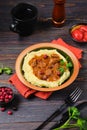 Roast beef stew with cranberries in sauce on a bed of mashed potatoes in a ceramic plate on a dark wooden background