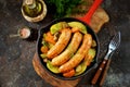 Roast Chicken sausages with potatoes, onions, carrots and mushrooms in a cast-iron pan. Top view. Royalty Free Stock Photo